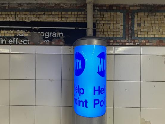 A blue MTA Help Point cylindrical sign lit up