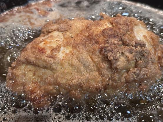 A piece of fried chicken is submerged in bubbling oil, showcasing a golden-brown, crispy coating.