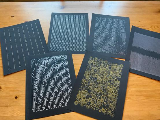 Various sheets of black paper featuring simple patterns in metallic gold and silver.