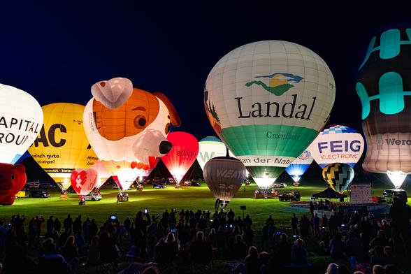 The picture shows hot air balloons in the evening. 
The lighting of the gas burners creates a special atmosphere.