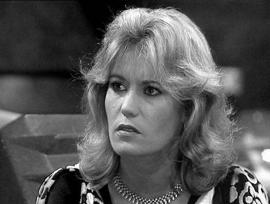 Claude 3.7 describes the image as: "This is a black and white image from a television production that appears to be from the late 1970s or early 1980s based on the styling. The image shows a person with voluminous, feathered blonde hair styled in a way typical of that era. They're wearing what looks like a patterned blouse or top with a pearl or beaded necklace. The expression appears somewhat serious or concerned, and the lighting creates a dramatic contrast typical of television productions from that period.

The image has the characteristic visual quality of British science fiction television productions from that time, with somewhat stark lighting and a studio-like setting. The monochrome presentation gives it a classic, vintage feel."

Blakes7Bot, version 3.9.30.