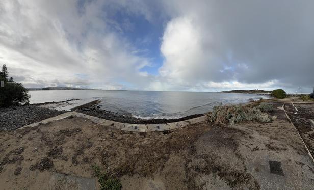 Panoramic daytime shot from the shoreline in Victor Harbour, South Australia, looking out over the ocean towards Port Elliot with some medium clouds overhead.