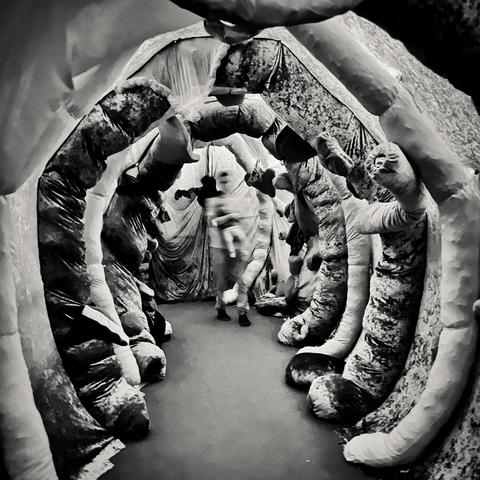 A surreal intestinal tunnel made of textured fabric, with a blurred figure moving through it, creating an eerie atmosphere. An artwork by Dafna Maimon presented here in black-and-white.
