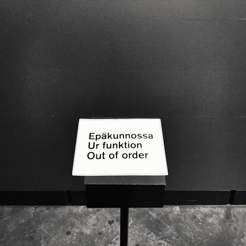 A sign on a stand reads "Out of order" in Finnish, Swedish and English against a dark LED-screen.