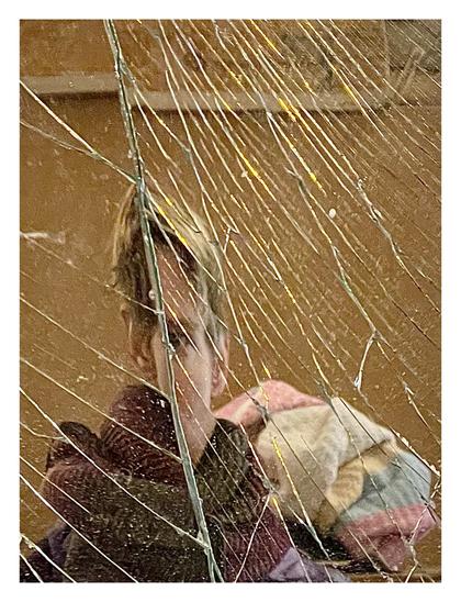 Selfportrait taken against a broken mirror: My ears, hair and a part of cheek and eye are visible. The rest is missing because of a crack. Textiles and a wooden wall in the background.