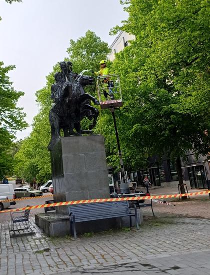 Hakkapeliittapatsas Lahden keskustassa. Kahta ratsukkoa esittävä patsas on ympäröity varoitusnauhalla ja huomiovaatteisiin pukeutunut mies pesee sitä letkulla henkilönostimen lavalta käsin.