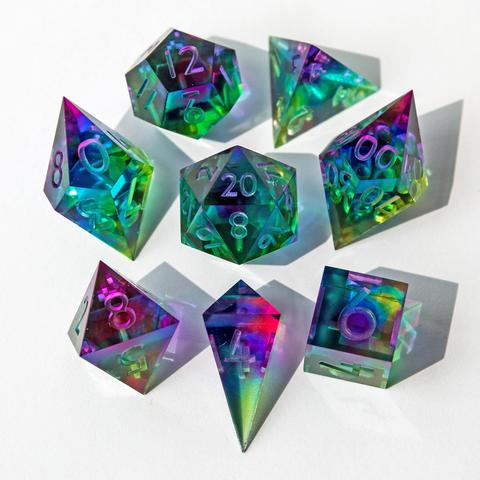 Ein 8-teiliges Würfelset in Blau, Lila und Gelb und Grüntönen. Das Set ist glasklar und durchsichtig und hat dadurch einen Glaseffekt. Die Würfel liegen auf weißem Untergrund und werden durch die Sonne erleuchtet, was zu Reflektionen auf dem Untergrund führt.  Auf dem Bild liegen alle Würfel mit der höchsten Seite nach oben und sind um den D20 herum angeordnet. Das Set besteht aus D4 Shard, D4 Pyramide, D6, D8, D10, D00, D12 und D20. Das Set ist noch Work in Progress, noch nicht geschliffen, poliert oder bemalt.
