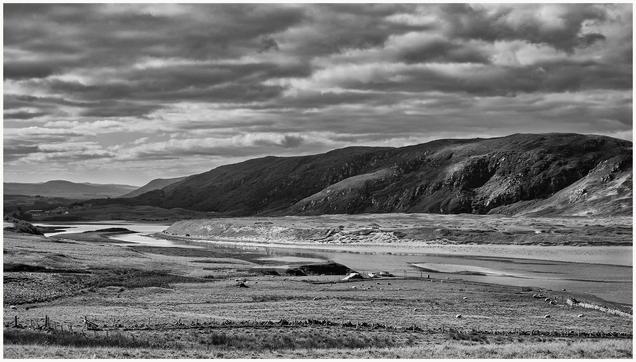A dramatic black and white landscape featuring rolling hills and a winding river. The scene includes a grassy plain with scattered sheep and a cloudy sky overhead.