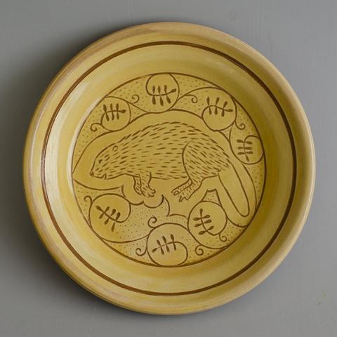 A yellow plate with a scratched drawing of a beaver in the middle, floating in the middle of a floral pattern of curling leaves.