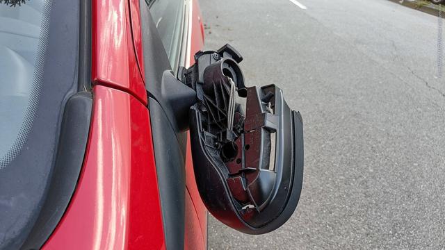 Ein Außenspiegel hängt beschädigt an einem roten Auto herunter. Betrüger zocken Autofahrer teilweise mit präparierten Außenspiegeln ab. (Foto: IMAGO, IMAGO/Michael Gstettenbauer)