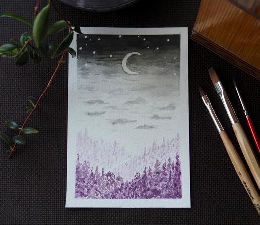 A photo of a postcard-sized watercolour painting of a nightly landscape on a dark brown table. At the bottom are purple woods, descending diagonally into a valley from both sides, dark at the front and getting paler further on. Above the woods is a pale sky with grey clouds, darkening gradually into a black sky at the top. There's a crescent moon and some stars in the sky.

Top left of the painting is a leafy vine growing from a pale purple pot, the bottom of which is slightly visible at the top. To the top right is an old wooden box. To the right are three brushes, two with flat heads and pale wooden handles, and one thin sharp brush with a red handle.