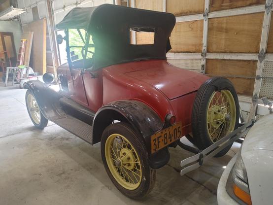 Rear driver side corner view of a 1927 Model T Runabout. Red body, black fenders, and straw colored wire wheels.