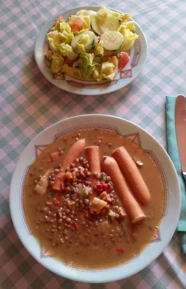Un plato de ensalada de lechuga, tomate y pepino.
Un plato hondo con lentejas y salchichas.