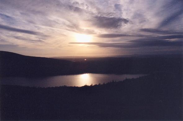 Dawn breaks through broken clouds over a mountain lake