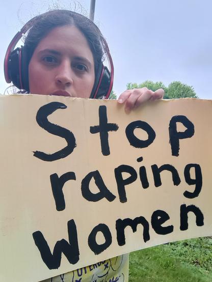 A woman carrying a sign in broad daylight. It reads: Stop Raping Women