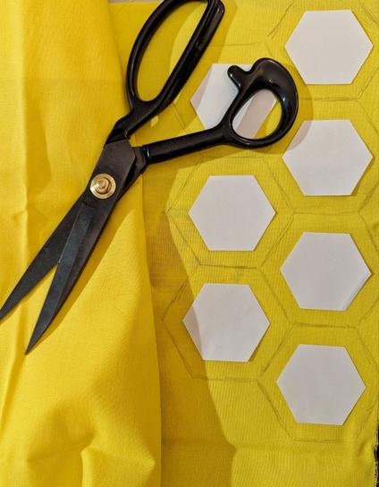 Gelber Stoff, scharze Stoffschere, darauf angezeichnet Hexagone zum Ausschneiden, mit schon aufgeklebten Papierschablonen.
