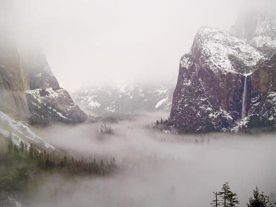 Storm Brewing

This is an image of Yosemite Valley captured at the Tunnel View parking lot as a winter storm was moving through the valley.
There is a heavy fog deep in the valley blocking out all but the closer features of the park
On the left is the base of El Capitan. All but the bottom is covered in fog.
On the right is Bridalveil Falls. Above the falls are some snow covered peaks.
Down in the valley you can see the tops of some of the taller trees sticking out above the fog.