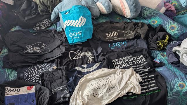 A pile of hackercamp shirts. HEU93 to EMF24. Also a Blahaj polycule.