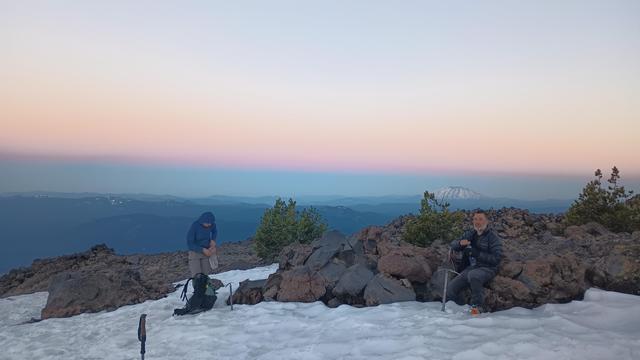 Two mountaineers rest on rocks with snow all around.