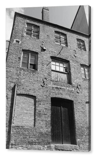 Black and white portrait photograph of an old brick built warehouse. The image is shown printed upon a box canvas.