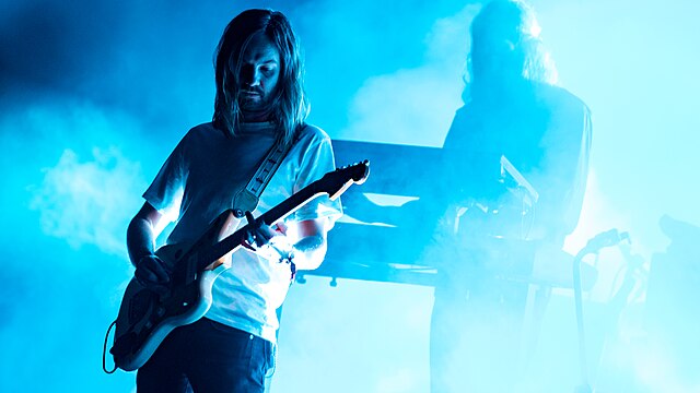 Tame Impala performing at Primavera Sound festival 2019. There is hazy vapours that are illuminated in blue while Kevin Parker plays his guitar.