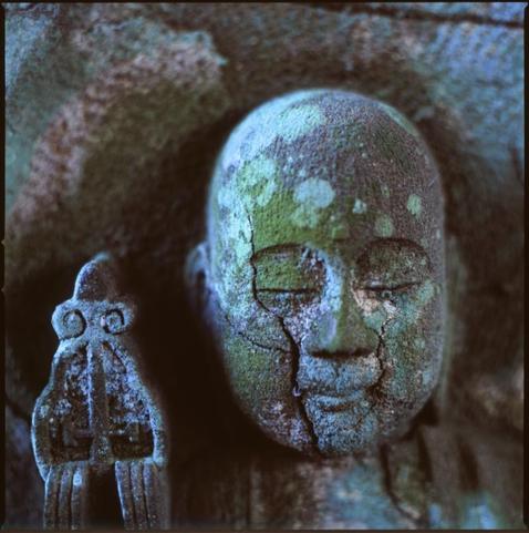 colour photograph of a small buddha, in low light. the colours tend to blue and green. out of focus highlights are almost a neon blue.