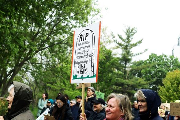 Photo of people gathered in a crowd and holding up signs opposed to Bill 5 in Guelph, Ontario.