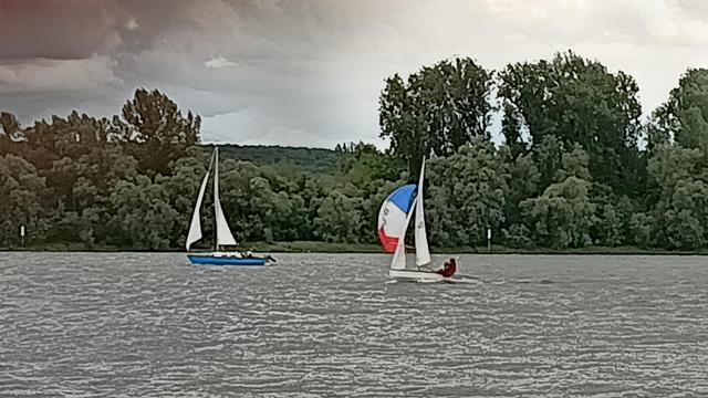 Ein blaues Boot mit weißen Segeln vor einem weißen Boot mit blauroten Segel