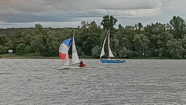 Ein blaues Boot mit weißen Segeln hinter einem weißen Boot mit blaurotem Segel
