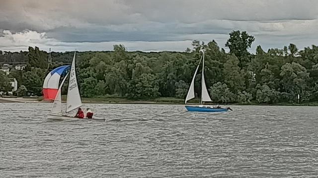 Ein blaues Boot mit weißen Segeln hinter einem weißen Boot mit blaurotem Segel