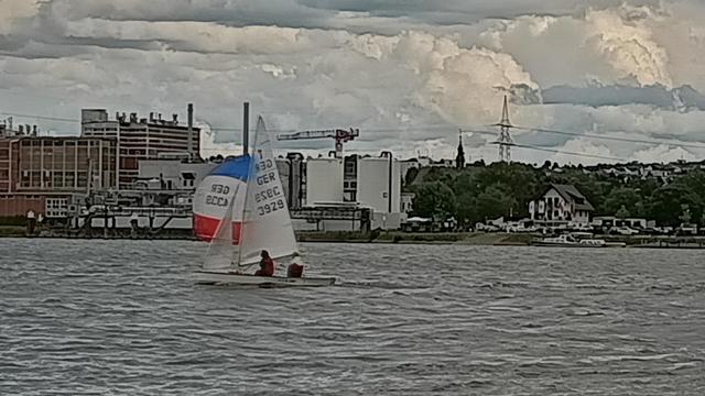 Ein weißes Boot mit blaurotem Segel vor einer Industriekulisse