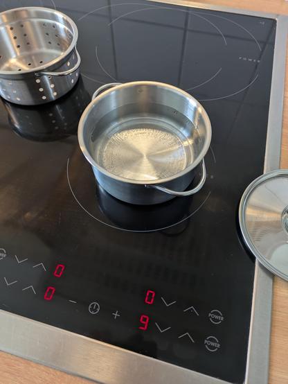 Auf der kleinsten Platte eines Herdes steht ein noch viel kleinerer Topf. Gefüllt mit Wasser und es bilden sich Luftbläschen am Topfboden. Die Herdanzeigen zeigt an, dass die Platte auf Stufe 9 steht.