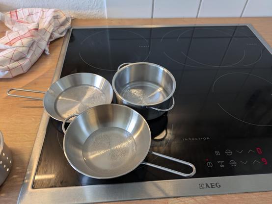 Der gleiche Topf aber nun zusammen mit zwei ähnlich großen Edelstahlpfannen. Stehen gemeinsam auf der größten Platte des Herds.