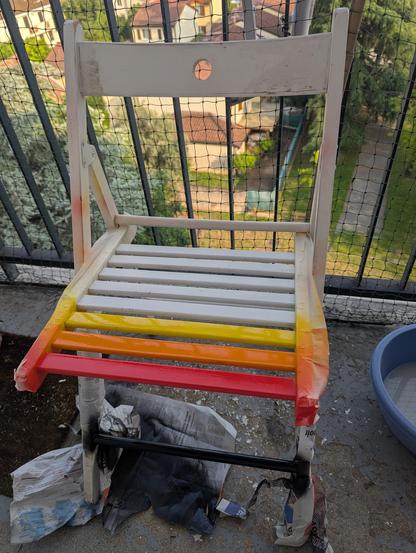 La chaise blanche avec les 3 premières lattes d'assise peintes en rouge, puis orange et enfin jaune.
Le barreau du bas où on peut mettre ses pieds a été peint en noir