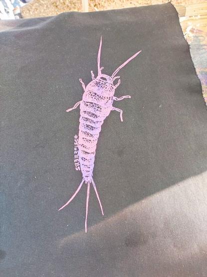 A print of a silverfish, in pink-purple on a dark fabric.