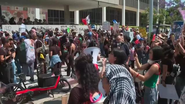 Still-frame of a live broadcast by Al Rojo Vivo from a crowd of protesters in LA. In the midst of a crowd is a red-and-black cargo bike with a small bucket.