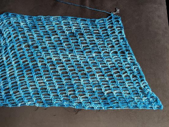 one end of a diagonal-lacework crochet wrap in variegated blue / teal / white, on a brown couch
