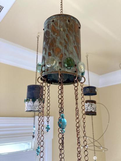 Photograph of tin-can mobiles decorated with copper and brass patina, lace, and beads hanging from a buttercup yellow ceiling.