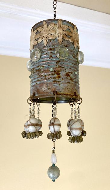 Photograph of a rusty tin-can mobile decorated with copper patina, lace, glass cabochons and beads.