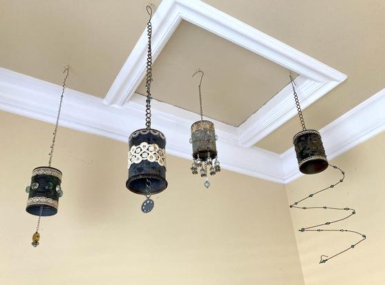 Photograph of tin-can mobiles decorated with copper and brass patina, lace, and beads hanging from a buttercup yellow ceiling.
