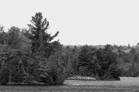 Eastern end of a small island (Slyvah Island) is heavily wooded with rock outcrops near the shoreline.