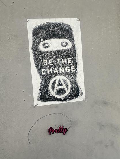 a faded black and white sticker with a drawing of a person in a balaclava with the words BE THE CHANGE and the letter A in a circle. below it is a tiny sticker with the word PRETTY in hot pink cursive letters