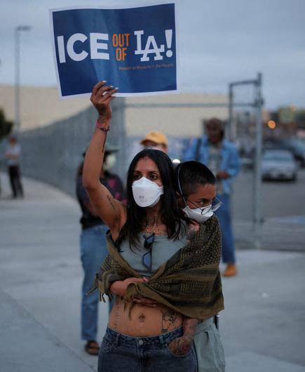 A photo from the reuters link in the post taken from an post from the /HT account in the post. The photo has been cropped to focus on on a woman holding up an "ICE out of LA!" sign with on hand. Here other hand is in her jeans pocket (like Alanis Morissette!!??). Another person is hugginer her from behind with a blanket around their shoulders.  With the crewcut and prescription glass I though the person with the blanket might be her gangly son but as he looks lonely and scared off into the distance. Both people have eyes that seem sad above white masks that look to me like a serious kind of disposable mask for the Covid pandemic...  Hopefully associating parts of Doors sone with this photo is not inappropriate vague memories just associate a feeling to "keep on risin'"...