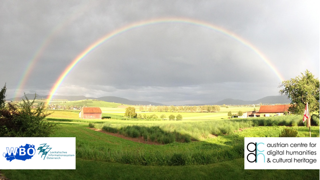 Das Bild zeigt eine weite ländliche Landschaft unter einem bewölkten Himmel, in dem sich ein leuchtender Doppelregenbogen spannt.
Im Vordergrund sieht man grüne Felder und Sträucher. Links und rechts stehen einzelne Bäume. In der Bildmitte stehen zwei kleine landwirtschaftliche Gebäude mit roten Dächern. Dahinter zieht sich eine leicht hügelige Landschaft mit weiteren Feldern, Bäumen und Dörfern bis zum Horizont. Im Hintergrund ist ein sanfter Bergrücken zu sehen.
Am Himmel erstreckt sich ein markanter Regenbogen von links nach rechts – mit einem schwächeren, zweiten Bogen darüber. Der Himmel ist überwiegend grau und wolkenverhangen, aber außerhalb des sichtbaren Bereichs brechen Sonnenstrahlen durch und beleuchten Teile der Landschaft, was den Regenbogen besonders intensiv erscheinen lässt.

In den unteren beiden Ecken sind zwei Logos eingefügt:
- Links unten die Logos des "Wörterbuchs der bairischen Mundarten in Österreich" (WBÖ) und des "Lexikalischen Informationssystems Österreich" (LIÖ).
- Rechts unten das Logo des "Austrian Centre for Digital Humanities & Cultural Heritage" (ACDH-CH).