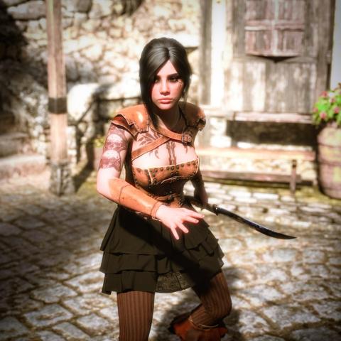 The image portrays a young woman in a dynamic, ready stance, appearing as a fantasy-style rogue or assassin. She has long dark hair tied back and wears a fitted, studded leather corset with matching shoulder and arm guards, giving her a rugged yet agile appearance. Her outfit includes a layered black skirt and striped brown leggings, along with sturdy leather boots—functional and suited for stealth or combat.

Her left arm is tattooed with intricate designs, including what looks like a skull motif, enhancing her fierce and battle-hardened look. In her right hand, she firmly grips a curved dagger, held low and ready. Her expression is intense and focused, as if she’s preparing to strike or defend herself.

The background features a rustic cobblestone street with a weathered wooden door, barrels, and stone walls, suggesting an old village or town setting. Bright sunlight casts sharp shadows, highlighting the detail in her costume and her tense, balanced posture.