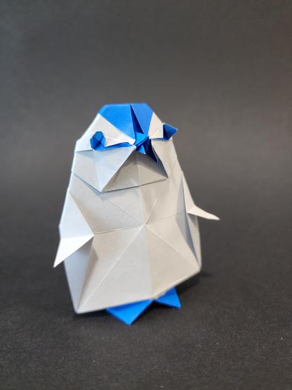 Un bébé pingouin en origami, plié dans un papier blanc et bleu. Son bec est entrouvert comme s'il attendait à manger.