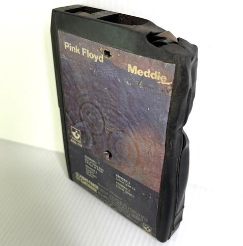 A photo of the same black plastic shell 8-track cartridge tape on a white background from a different angle. Here the melted/distorted edges at the top and side can been seen more prominently.