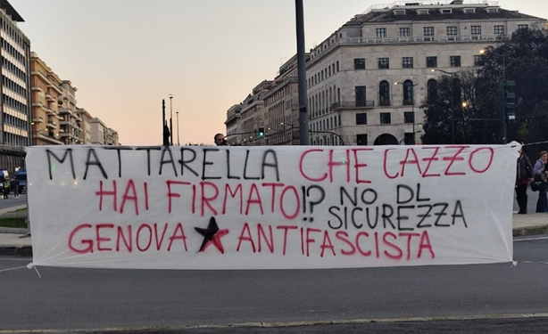 Scritta nera e rossa su uno striscione bianco: "Mattarella che cazzo hai firmato!? No dl sicurezza
Genova (stella nera e rossa) antifascista"
