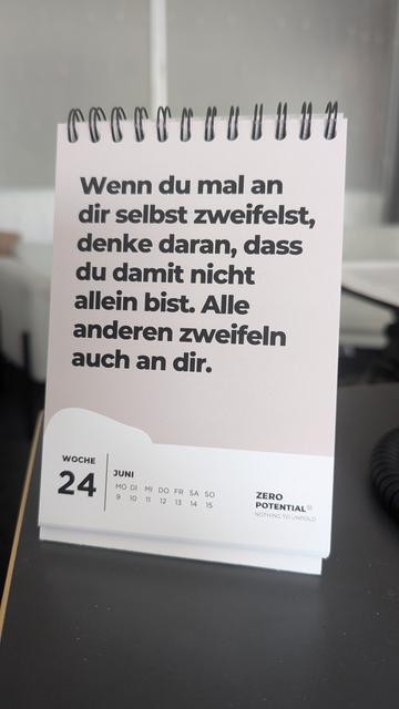 Das Bild zeigt einen Tischkalender mit Spiralbindung, der auf Woche 24 eingestellt ist (9. bis 15. Juni). Auf der Kalenderseite steht ein motivierender Spruch auf Deutsch:  
"Wenn du mal an dir selbst zweifelst, denke daran, dass du damit nicht allein bist. Alle anderen zweifeln auch an dir."

Unten rechts auf der Seite steht: "ZERO POTENTIAL® NOTHING TO UNFOLD."