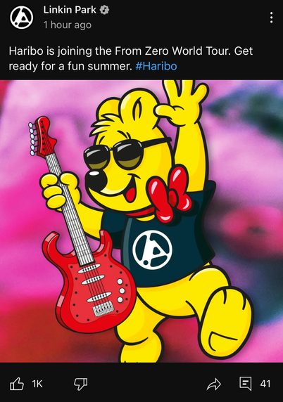 Ein Post aus Linkin Parks YouTube Kanal. Man sieht einen Haribo Goldbär, der ein Linkin Park Hemd und Sonnenbrille trägt und eine Gitarre hält. Auf dem Post liest man auf English: „Haribo macht mit bei der From Zero World Tour. Bereitet euch auf einen tollen Sommer vor. #Haribo“